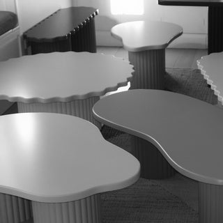 A set of modern cloud-shaped coffee tables with scalloped tops and ribbed pedestal bases, shown in a monochrome interior setting.