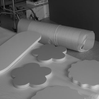 White molded foam pieces, including flower-shaped and scalloped pieces, alongside a rolled sheet, photographed on a tabletop with a dark background.