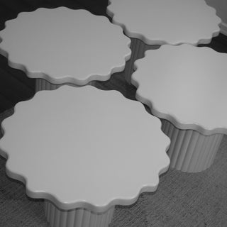 Four white scalloped-edge pedestal tables arranged together on a gray textured floor.