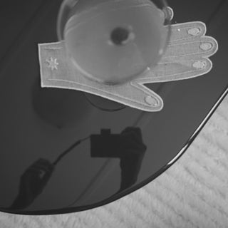 A close-up of a clear, glove-shaped transparent object with embroidered details and a small star motif, resting on a glossy dark surface with a soft textured fabric background.