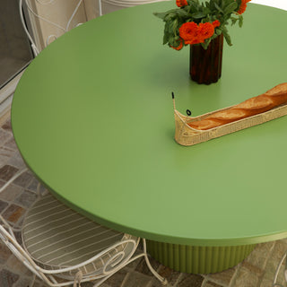 Green round table with a vase of flowers and bread basket on a tiled floor.