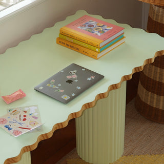 Light green desk with a laptop, books, and stationery items in a room.