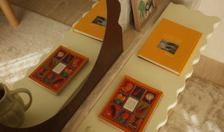 Three books with colorful covers on a white surface, with a cup and wooden chair in the background.